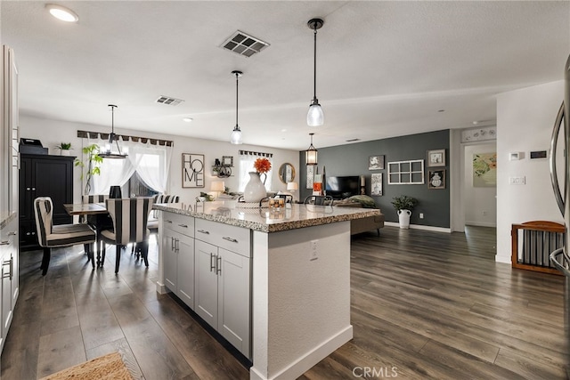 kitchen with decorative light fixtures, dark hardwood / wood-style floors, light stone countertops, and a center island