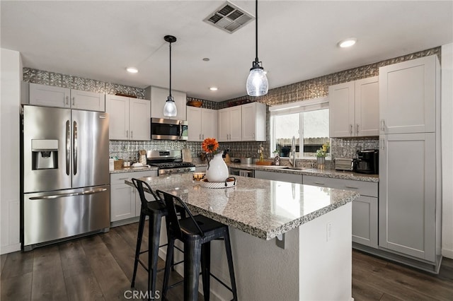 kitchen with hanging light fixtures, dark hardwood / wood-style floors, a kitchen island, stainless steel appliances, and light stone countertops