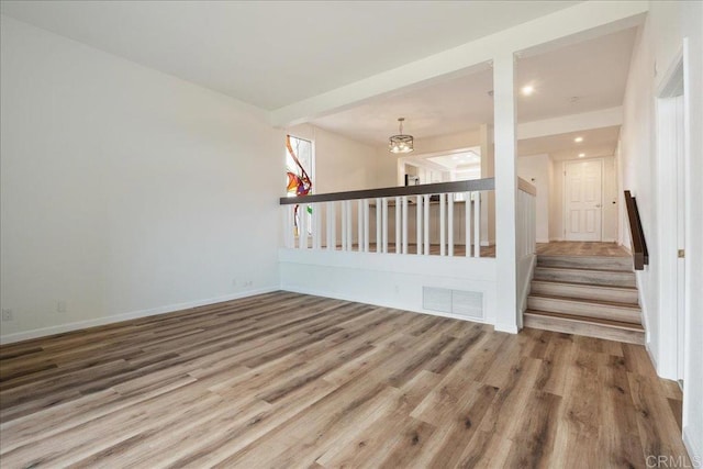 unfurnished room featuring stairs, wood finished floors, visible vents, and baseboards