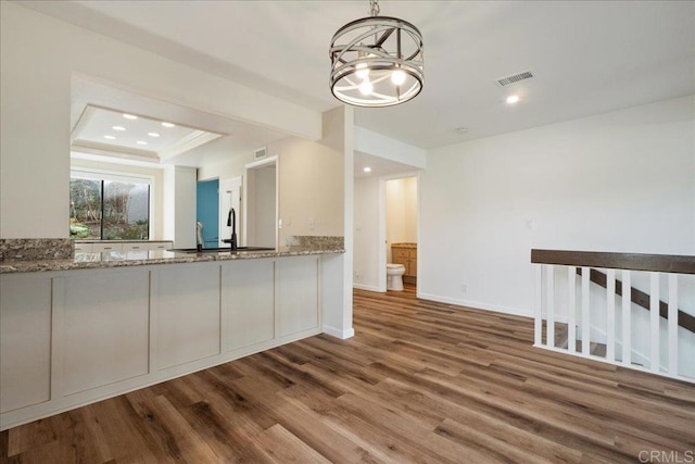 kitchen featuring light stone counters, decorative light fixtures, visible vents, white cabinets, and wood finished floors