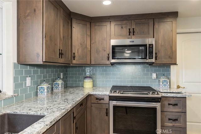 kitchen featuring stainless steel appliances, tasteful backsplash, and light stone countertops