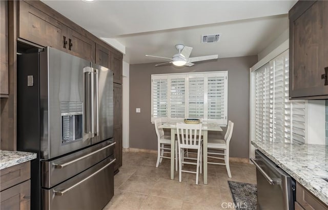 kitchen with ceiling fan, dark brown cabinets, stainless steel appliances, light stone counters, and light tile patterned flooring