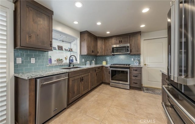 kitchen with dark brown cabinetry, sink, light stone counters, light tile patterned floors, and stainless steel appliances