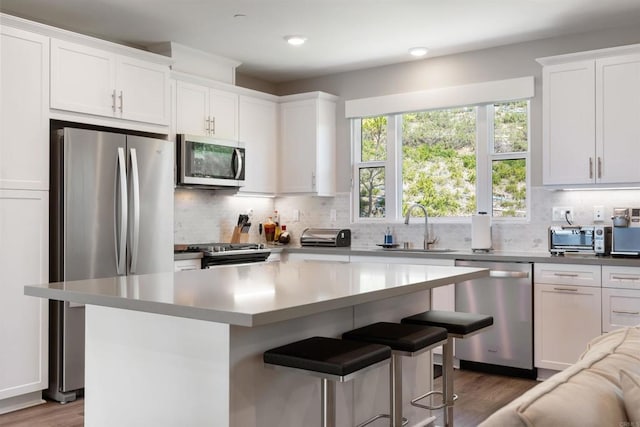 kitchen with sink, a center island, appliances with stainless steel finishes, white cabinets, and backsplash