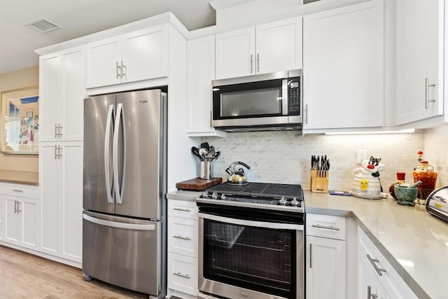 kitchen with stainless steel appliances, white cabinetry, backsplash, and light wood-type flooring