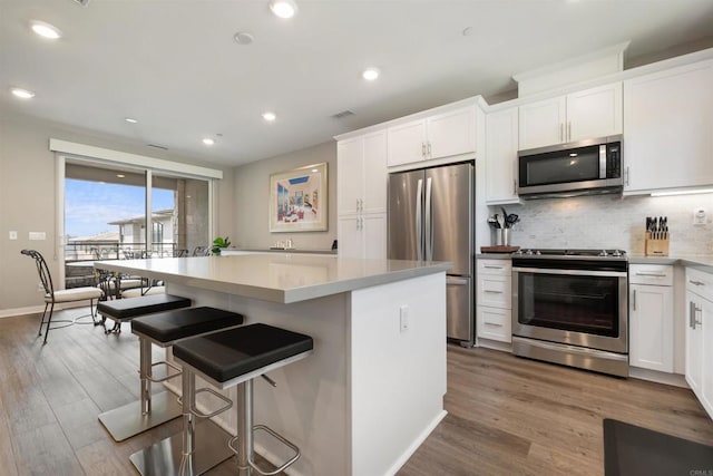 kitchen with a breakfast bar area, stainless steel appliances, tasteful backsplash, white cabinets, and a kitchen island