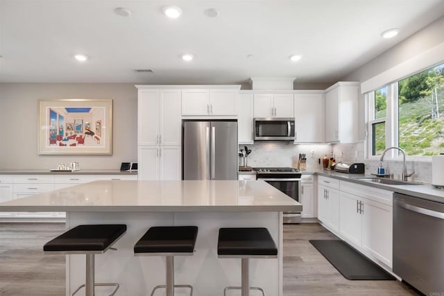 kitchen with white cabinetry, sink, stainless steel appliances, and a kitchen island