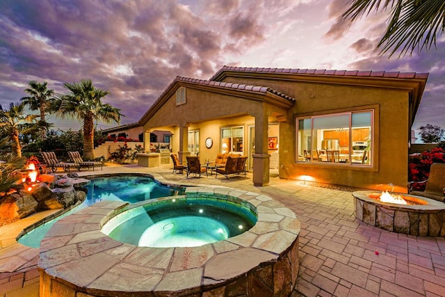 pool at dusk with an in ground hot tub, a patio area, and a fire pit