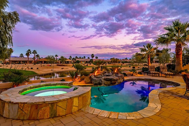 pool at dusk featuring an in ground hot tub and a patio area