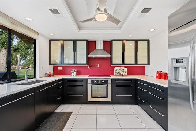 kitchen with appliances with stainless steel finishes, sink, light tile patterned floors, a raised ceiling, and wall chimney exhaust hood