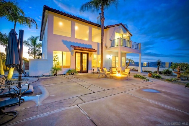 back house at dusk featuring french doors, a patio, a balcony, and an outdoor fire pit