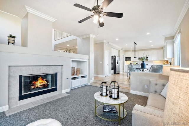 living room with crown molding, light carpet, built in features, a tile fireplace, and ceiling fan