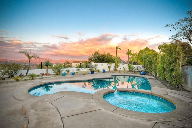 pool at dusk featuring a mountain view and an in ground hot tub