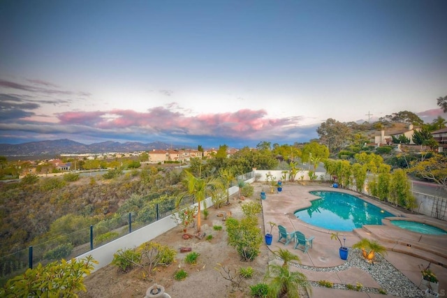 pool at dusk featuring an in ground hot tub, a mountain view, and a patio