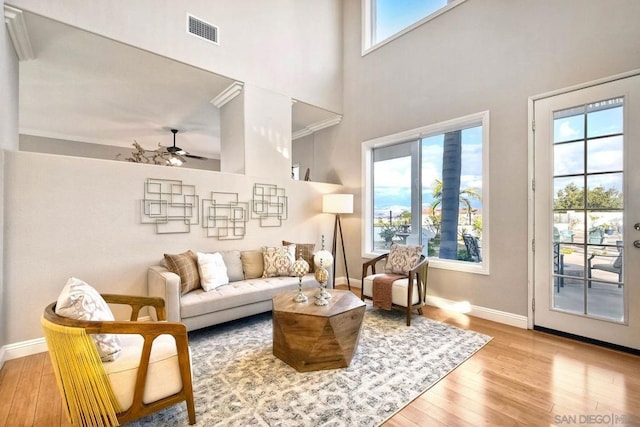 living room with a high ceiling, ceiling fan, and light wood-type flooring