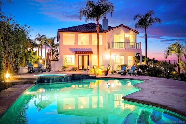 back house at dusk featuring a balcony, an outdoor fire pit, a pool with hot tub, and a patio area