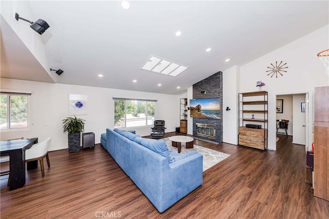 living room featuring a stone fireplace, dark wood-type flooring, high vaulted ceiling, and a skylight