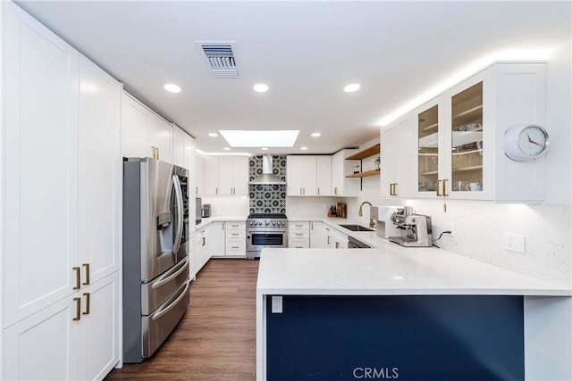 kitchen featuring sink, white cabinetry, kitchen peninsula, stainless steel appliances, and wall chimney range hood