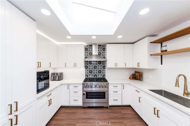 kitchen with stainless steel range, wall chimney exhaust hood, sink, and white cabinets