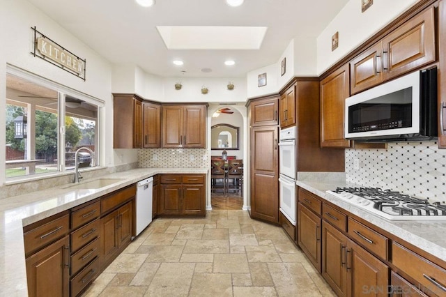 kitchen featuring a skylight, tasteful backsplash, sink, light stone counters, and white appliances