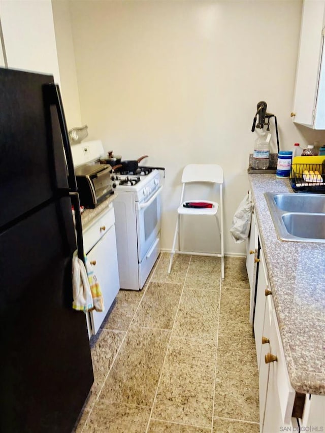 kitchen with white cabinetry, black fridge, sink, and white gas range oven