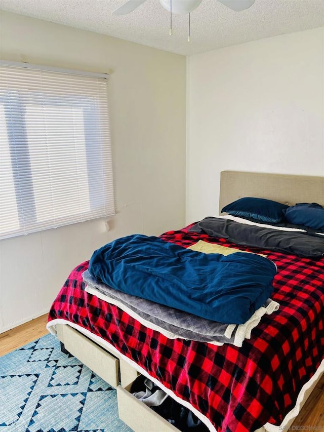 bedroom featuring ceiling fan, hardwood / wood-style floors, and a textured ceiling