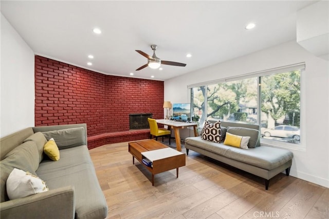 living room featuring a fireplace, light hardwood / wood-style flooring, ceiling fan, and brick wall