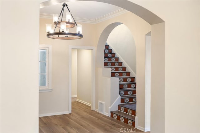 stairs with an inviting chandelier, ornamental molding, and hardwood / wood-style floors