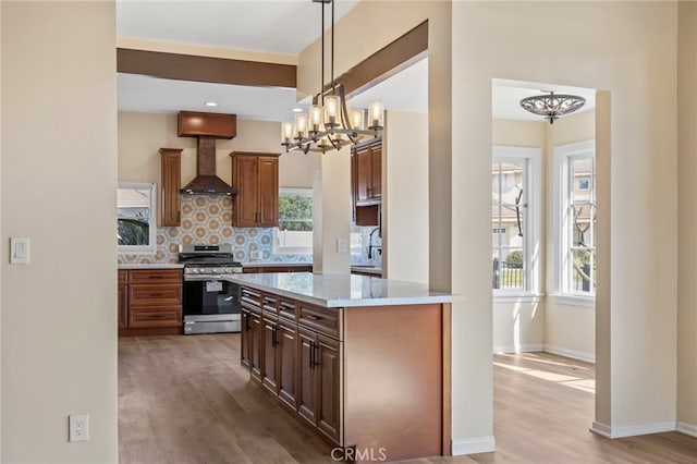 kitchen with pendant lighting, wall chimney range hood, tasteful backsplash, gas range, and light wood-type flooring