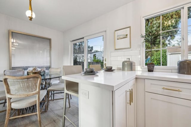 kitchen featuring hanging light fixtures, decorative backsplash, light hardwood / wood-style flooring, and white cabinets