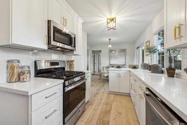 kitchen with tasteful backsplash, hanging light fixtures, light wood-type flooring, stainless steel appliances, and white cabinets