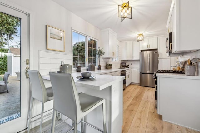 kitchen with stainless steel appliances, a kitchen bar, decorative backsplash, and white cabinets