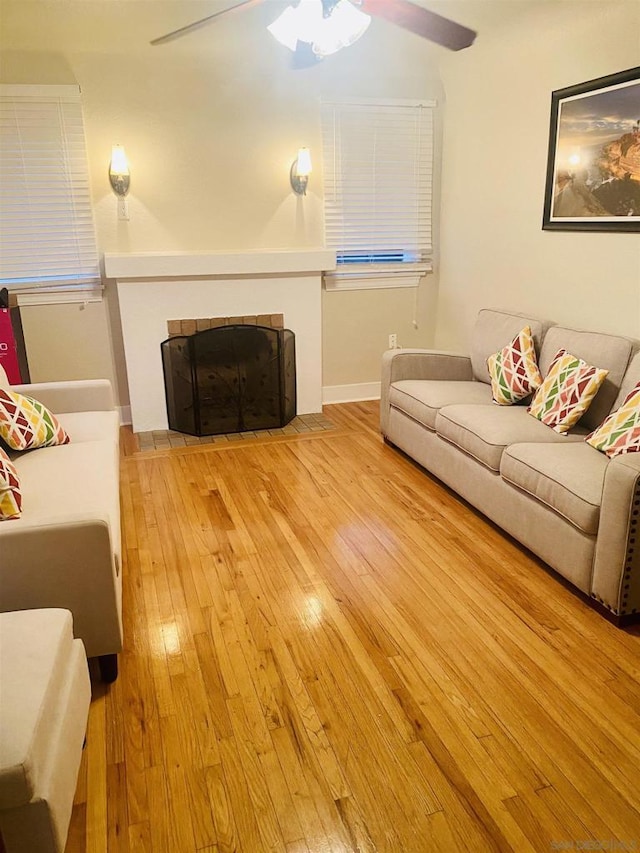 living room featuring a tile fireplace, ceiling fan, and light hardwood / wood-style floors