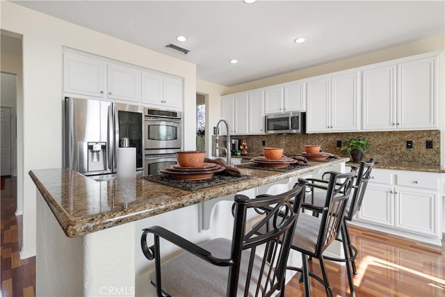 kitchen with backsplash, a breakfast bar, white cabinets, and appliances with stainless steel finishes