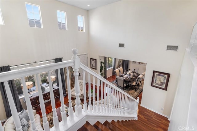 stairway with wood-type flooring and a towering ceiling