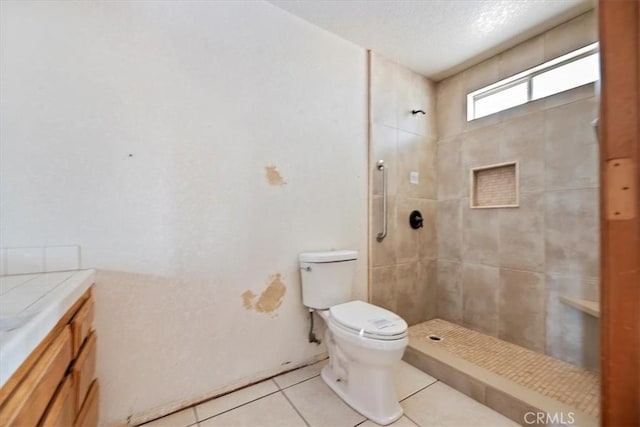 bathroom with tile patterned flooring, vanity, tiled shower, and toilet