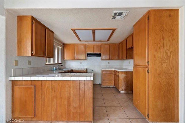 kitchen featuring sink, tile counters, kitchen peninsula, and light tile patterned floors