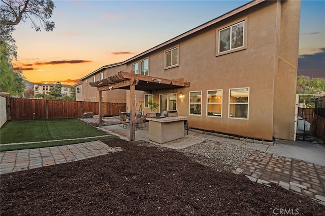 back of property at dusk with stucco siding, a fenced backyard, a patio, and a pergola