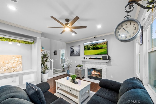 living area with ornamental molding, a ceiling fan, a stone fireplace, wood finished floors, and baseboards