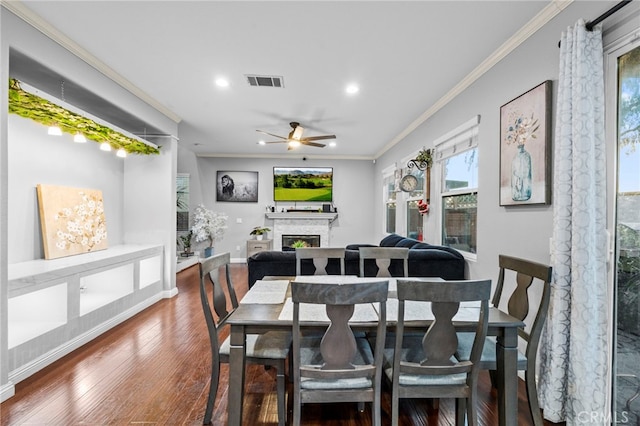 dining space featuring dark wood-style flooring, visible vents, baseboards, a lit fireplace, and crown molding