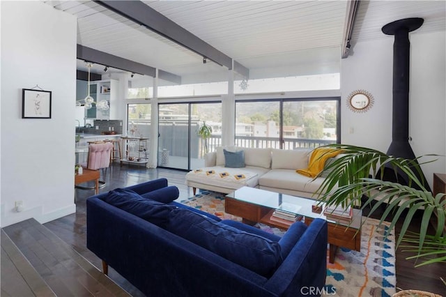 living room featuring beamed ceiling, a healthy amount of sunlight, dark wood-type flooring, and a wood stove