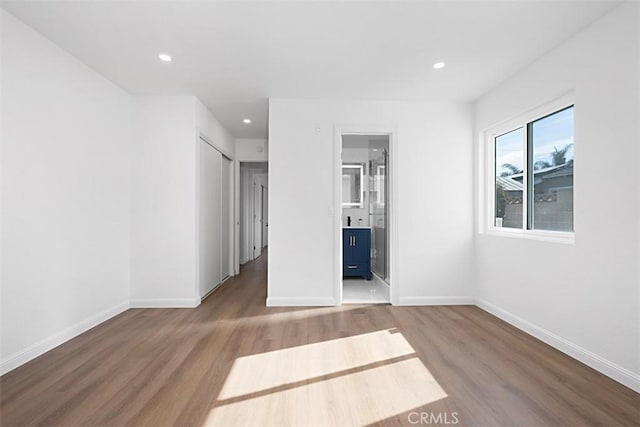 unfurnished bedroom with ensuite bathroom and hardwood / wood-style floors