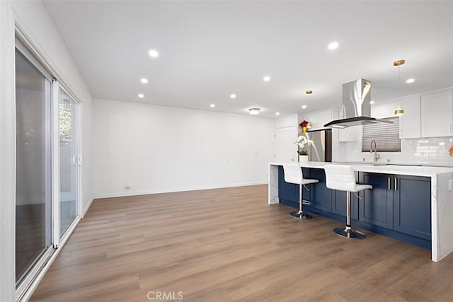 kitchen featuring a kitchen bar, white cabinetry, island range hood, stainless steel fridge, and pendant lighting