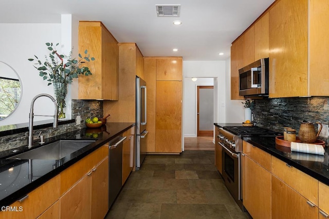 kitchen with dark stone countertops, sink, decorative backsplash, and premium appliances