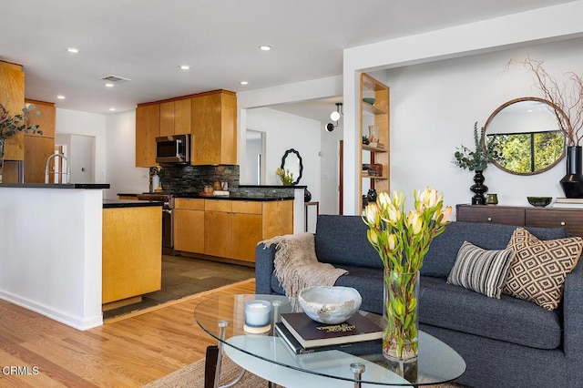 kitchen with sink, light wood-type flooring, kitchen peninsula, stainless steel appliances, and decorative backsplash