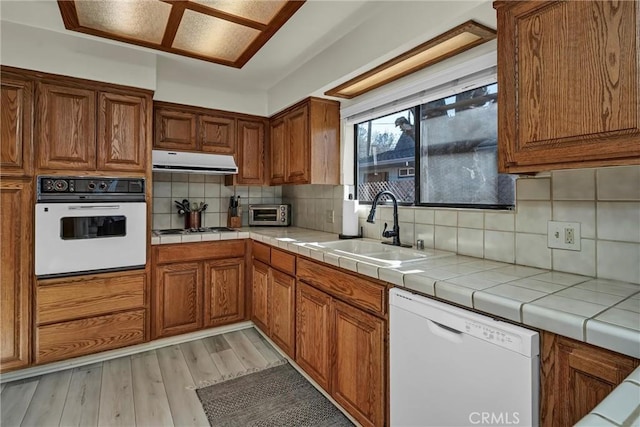 kitchen with sink, tile countertops, white appliances, light hardwood / wood-style floors, and decorative backsplash