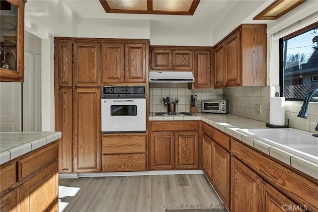 kitchen with white appliances, tile counters, light hardwood / wood-style flooring, and backsplash