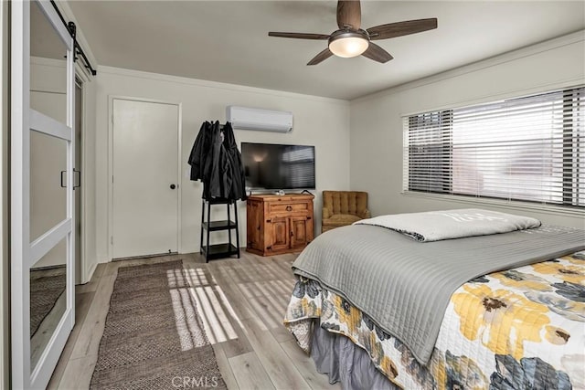 bedroom with light hardwood / wood-style flooring, ornamental molding, a wall unit AC, ceiling fan, and a barn door