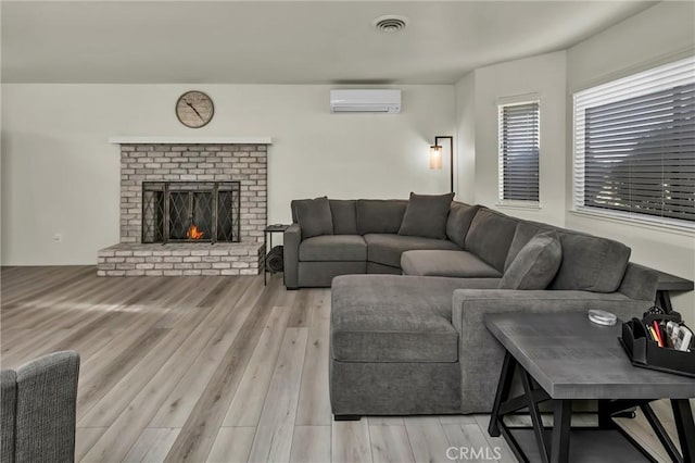 living room with a brick fireplace, a wall mounted AC, and light wood-type flooring