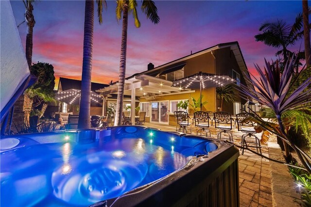 pool at dusk featuring a hot tub, a patio area, and a pergola